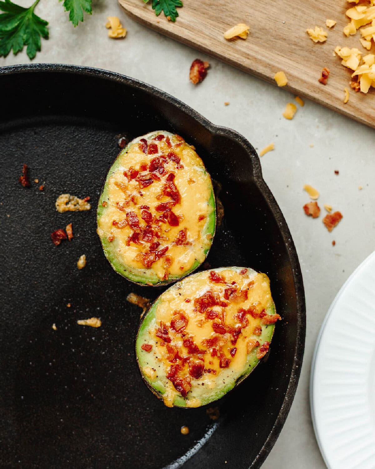 An avocado sliced in half, filled with egg, bacon, and cheese and cooked in a skillet.