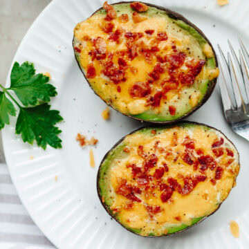 Cheesy bacon and egg stuffed avocados on a white plate.
