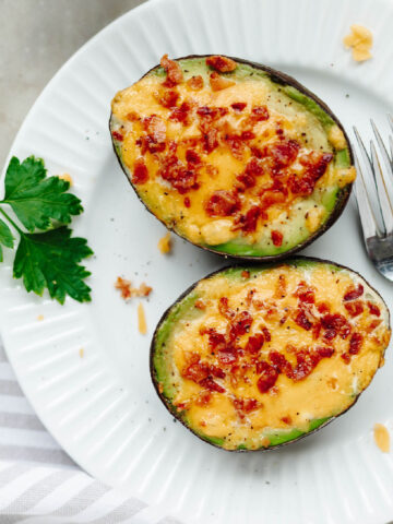 Cheesy bacon and egg stuffed avocados on a white plate.