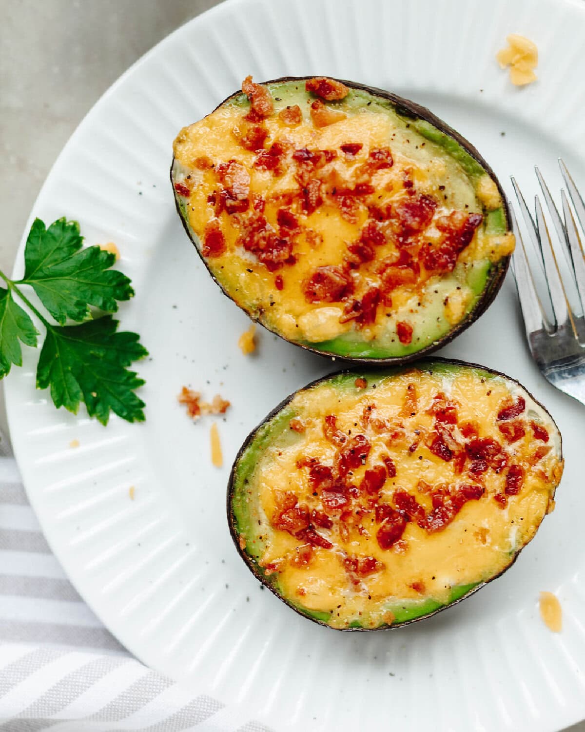 Cheesy bacon and egg stuffed avocados on a white plate.