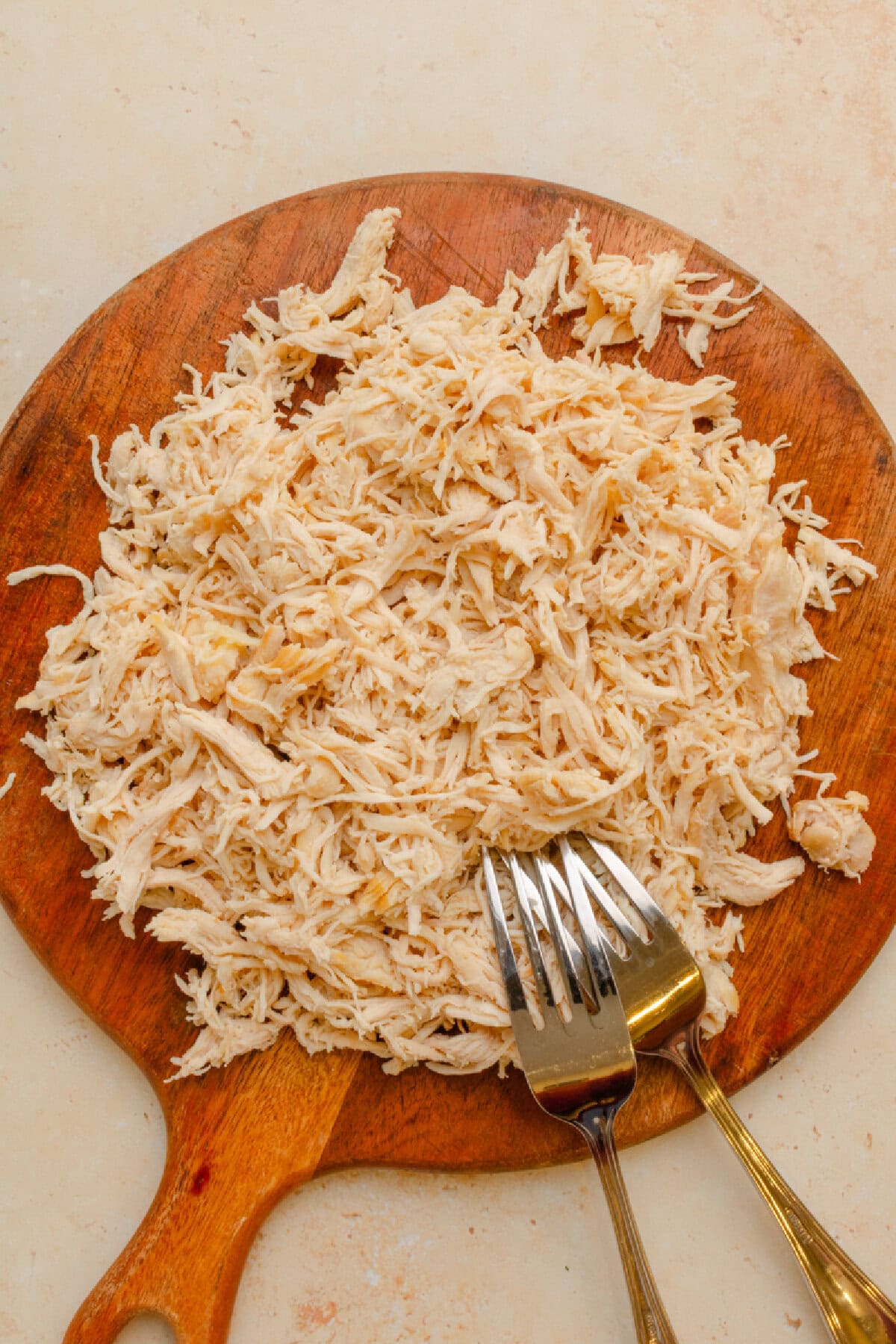 Shredded chicken on a wood cutting board with two forks.