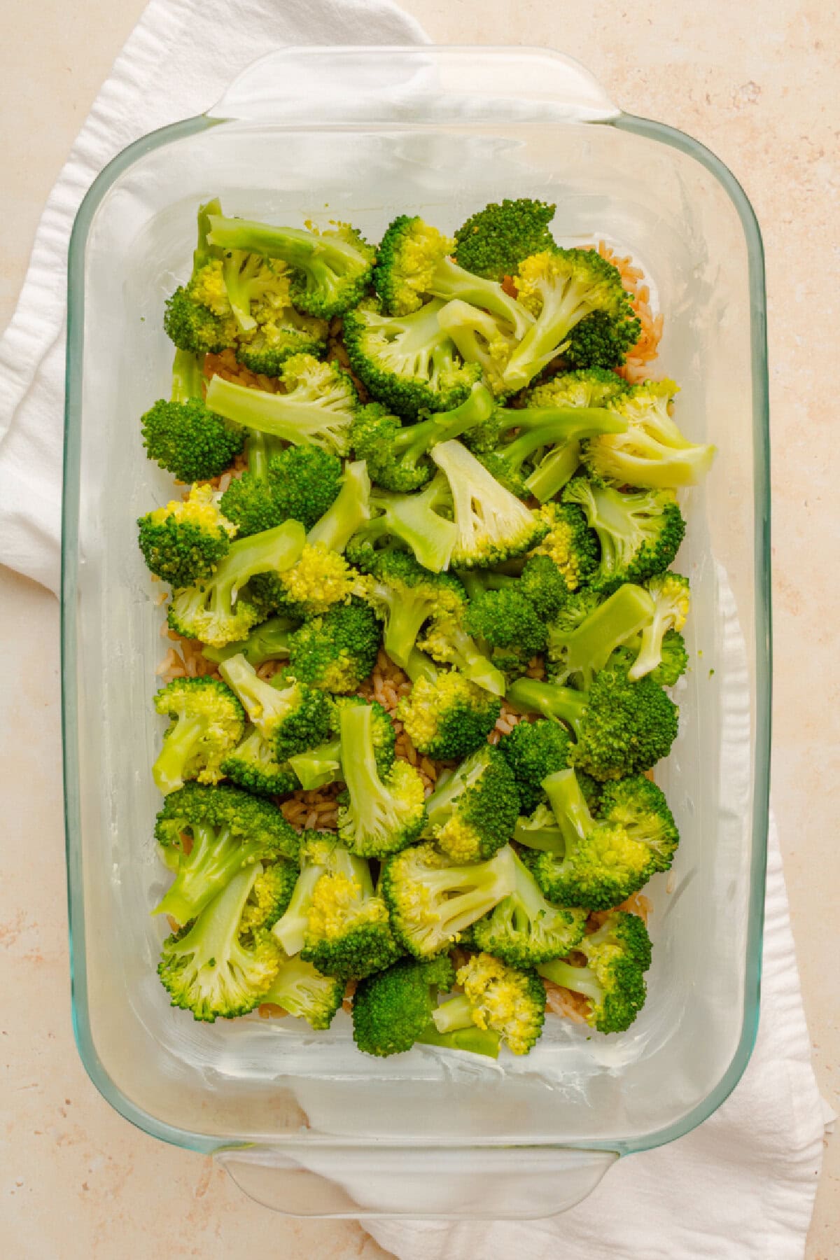 Cooked broccoli spread on top of cooked brown rice in a baking pan.