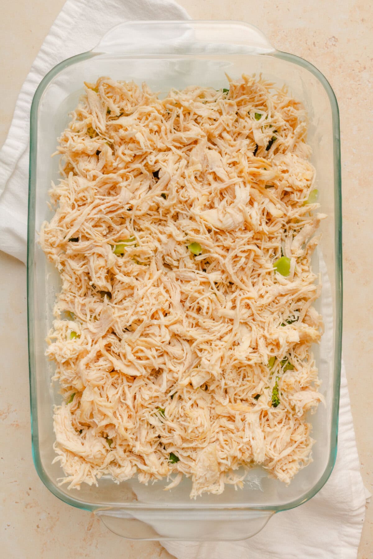 Shredded chicken on top of cooked broccoli and brown rice in a baking dish.