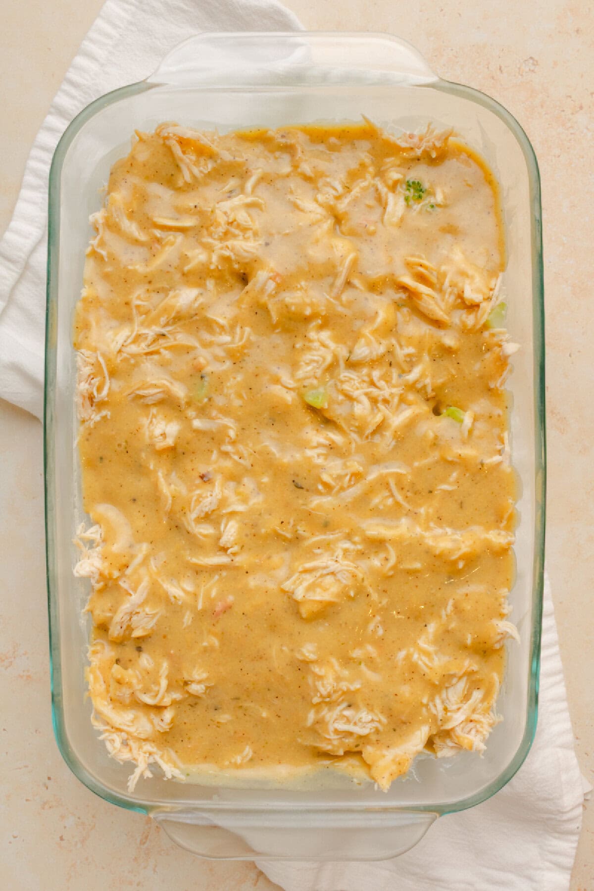 Cream of chicken soup mixture poured over chicken, broccoli, and rice in a casserole pan.