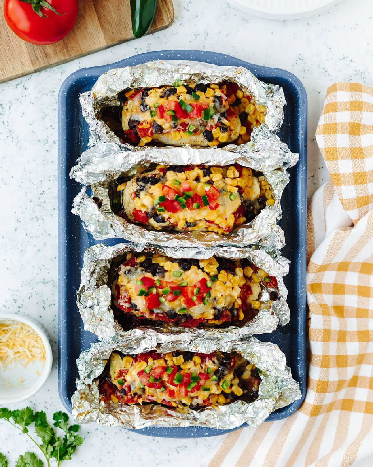 Four foil packets filled with chicken, beans, tomatoes, and cheese.