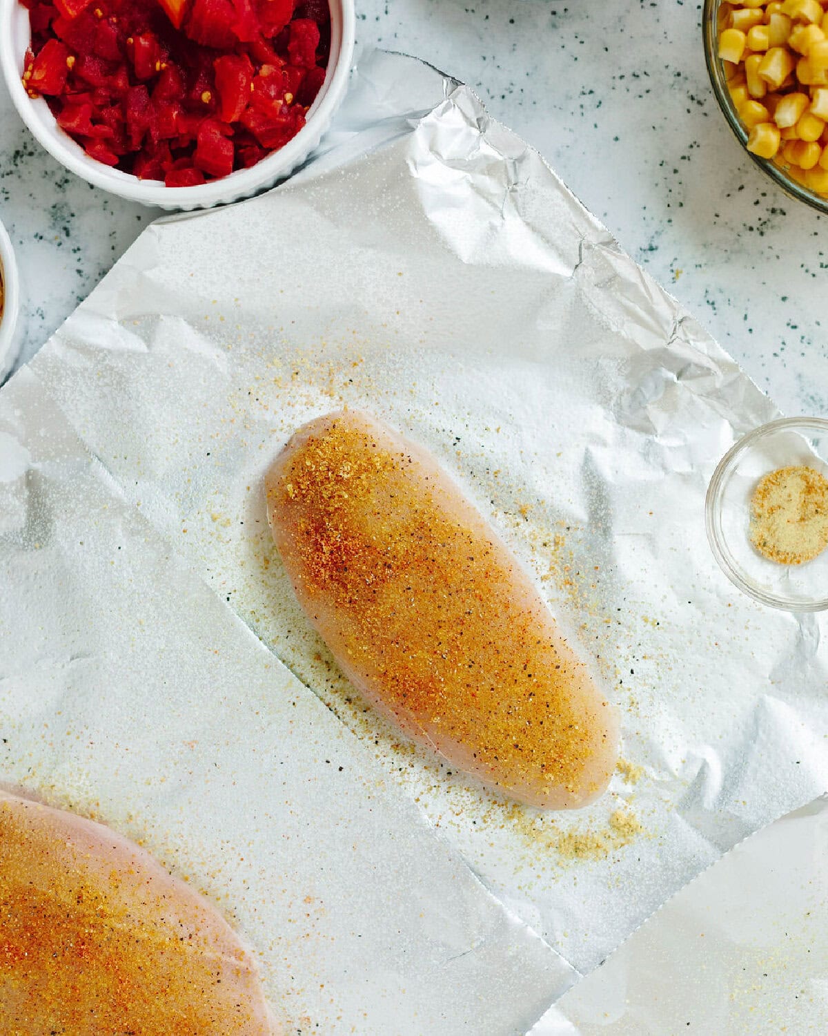 A chicken breast seasoned on top of a piece of aluminum foil.