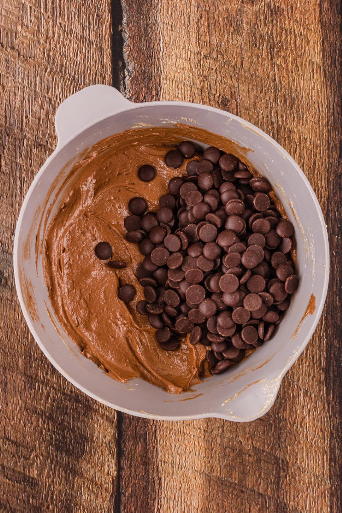 Chocolate chips folded into cookie dough batter in a mixing bowl.