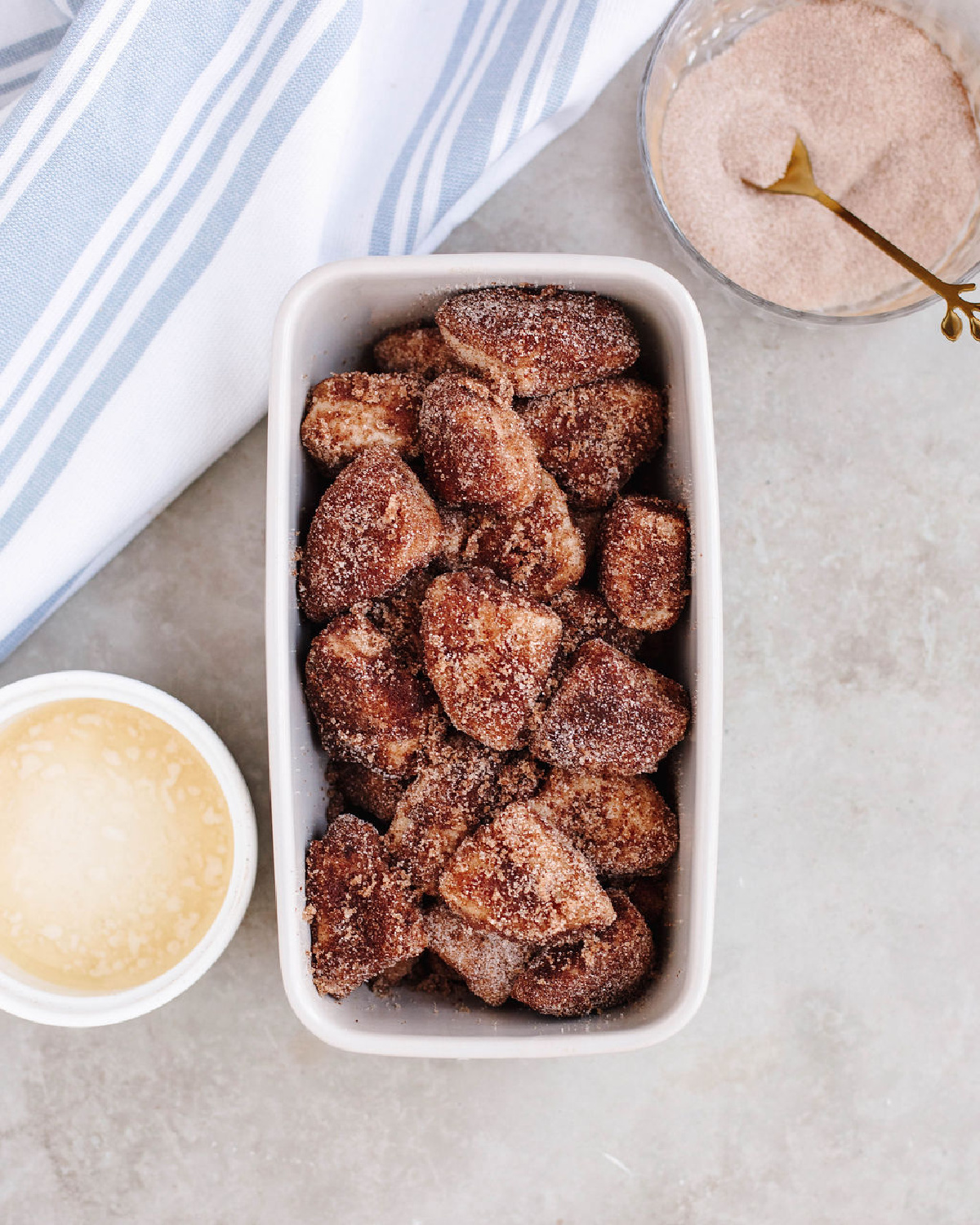 Cinnamon sugar coated biscuit pieces in a white loaf pan ready to bake.
