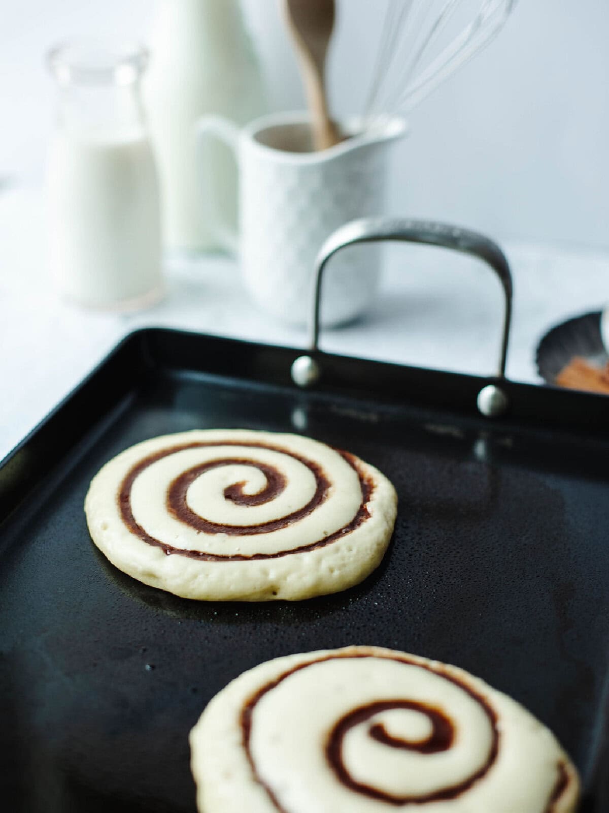 Homemade pancakes with a cinnamon mixture on a black griddle.