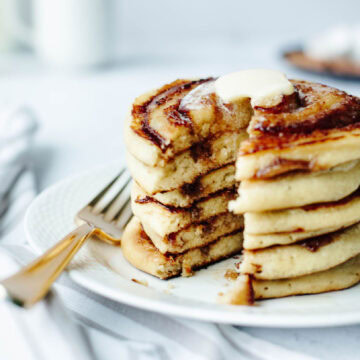 A stack of cinnamon swirl pancakes on a white plate with butter and a fork.