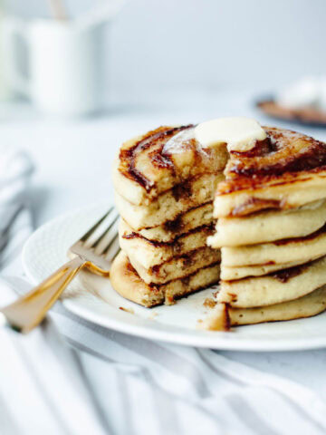 A stack of cinnamon swirl pancakes on a white plate with butter and a fork.