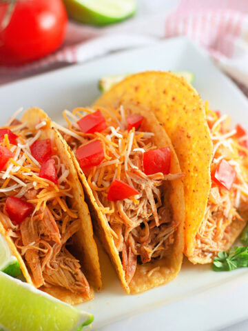 A white plate with three crunchy tacos filled with Ranch seasoned chicken from the slow crockpot.