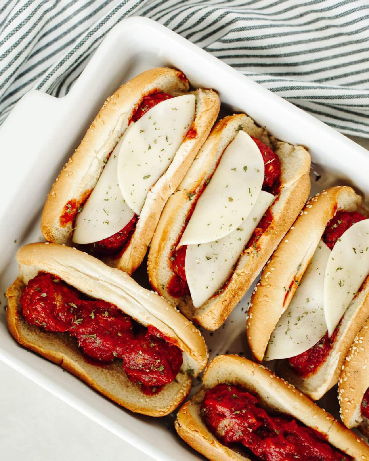 Provolone cheese on top of homemade meatballs in hoagie rolls with marinara sauce.