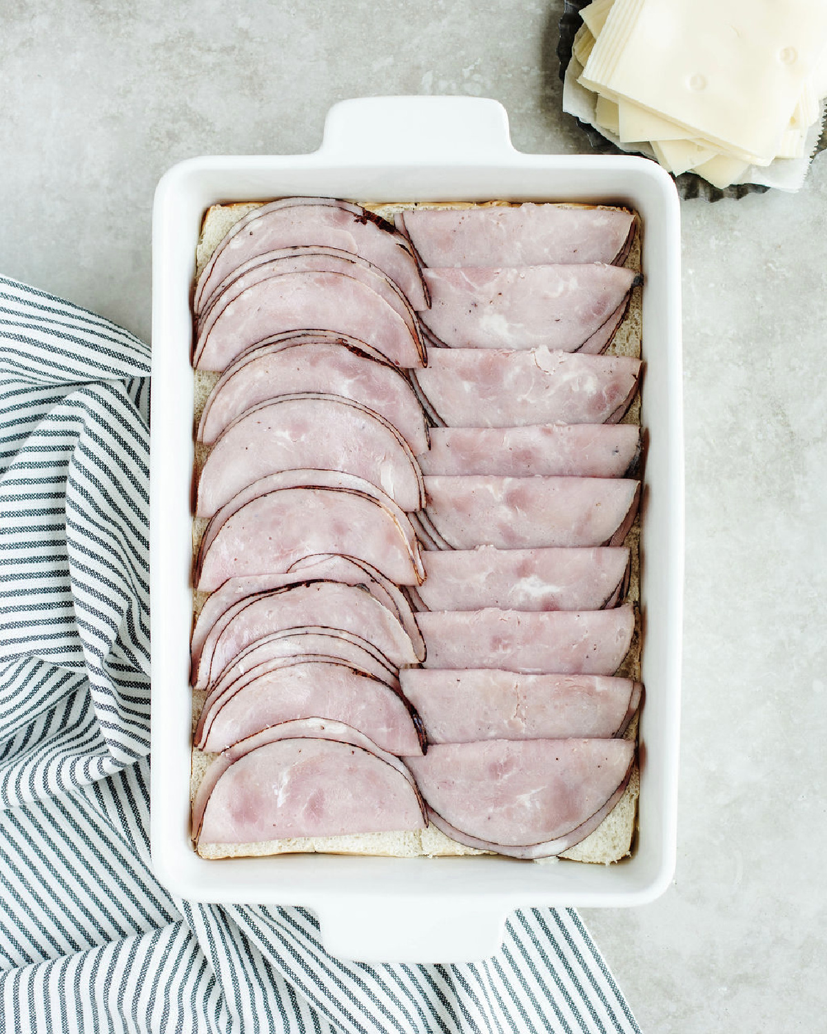 Sliced ham placed on top of Hawaiian rolls in a white baking dish.