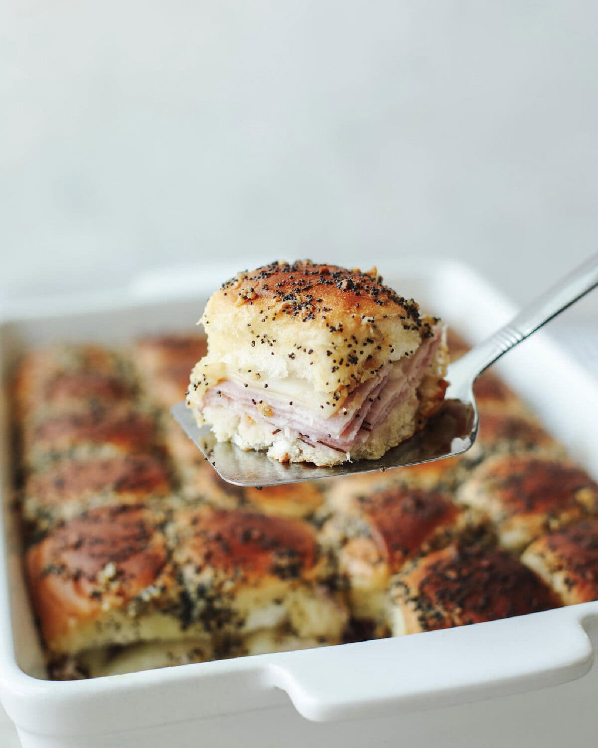 A metal spatula serving a funeral sandwich from a white baking dish.