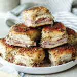 Baked ham and cheese sliders stacked on a white plate.