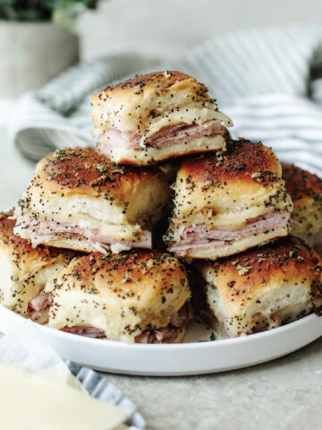 Baked ham and cheese sliders stacked on a white plate.