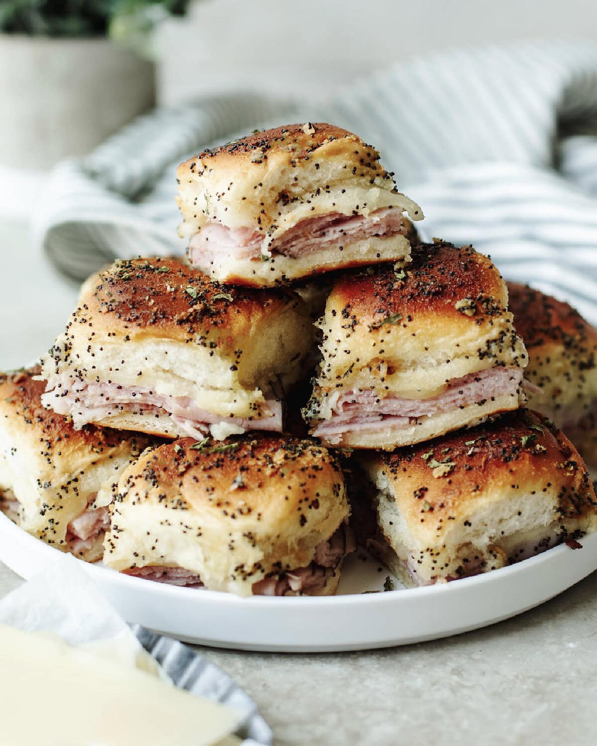 Baked ham and cheese sliders stacked on a white plate.
