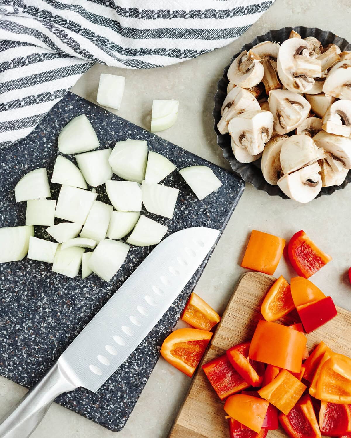 A cutting board with diced onions, peppers, and mushrooms.