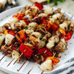 Marinated chicken kabobs grilled and placed on a white serving platter.