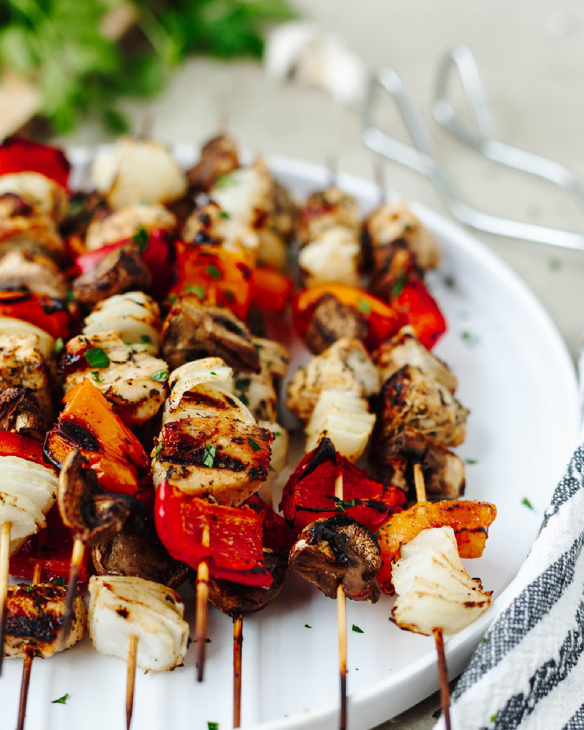 Garlic herb chicken kabobs grilled and stacked on a white platter.