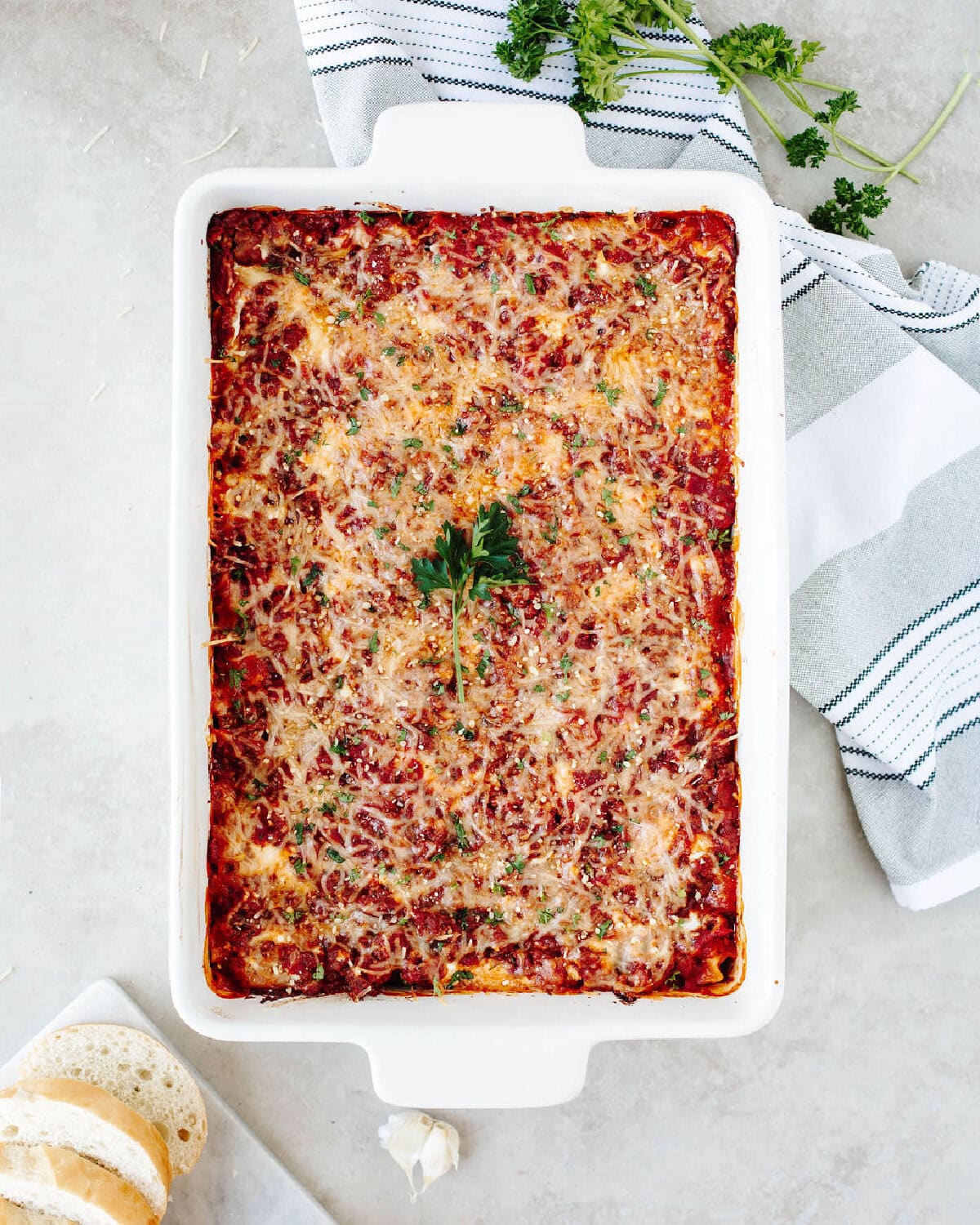 Freshly baked homemade lasagna in a white baking dish topped with melted cheese and parsley.