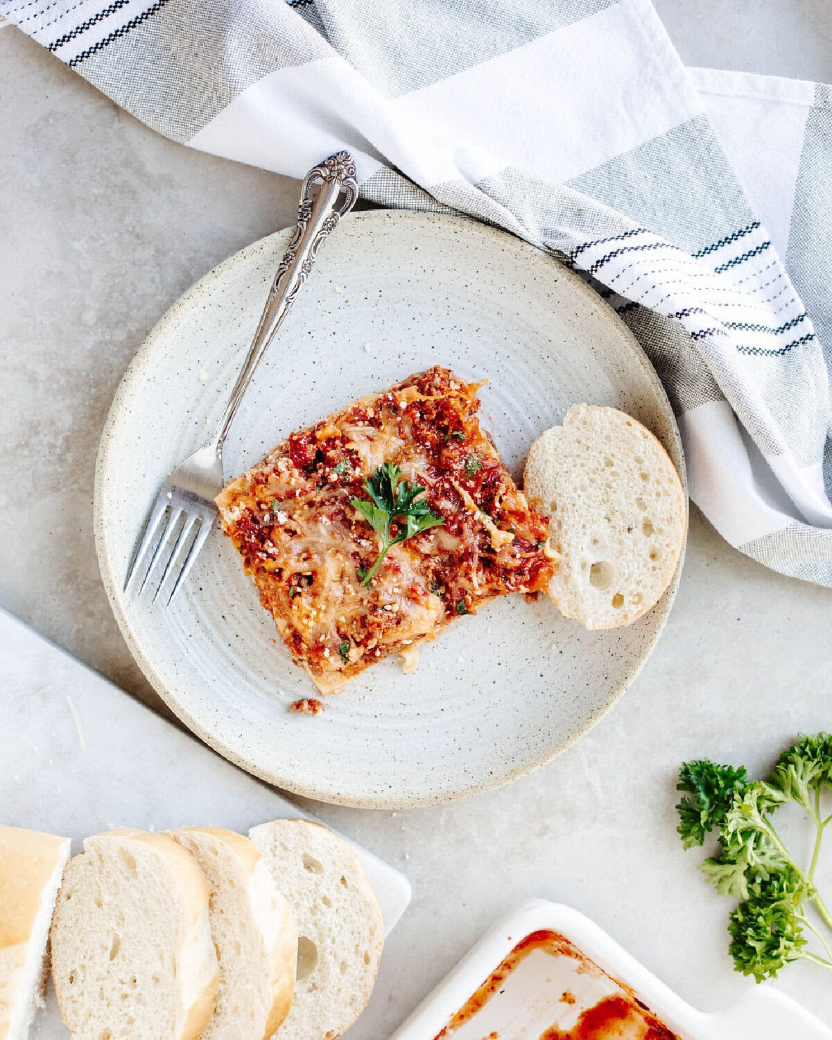 Grandma's lasagna recipe served on a plate with slices of crusty bread.