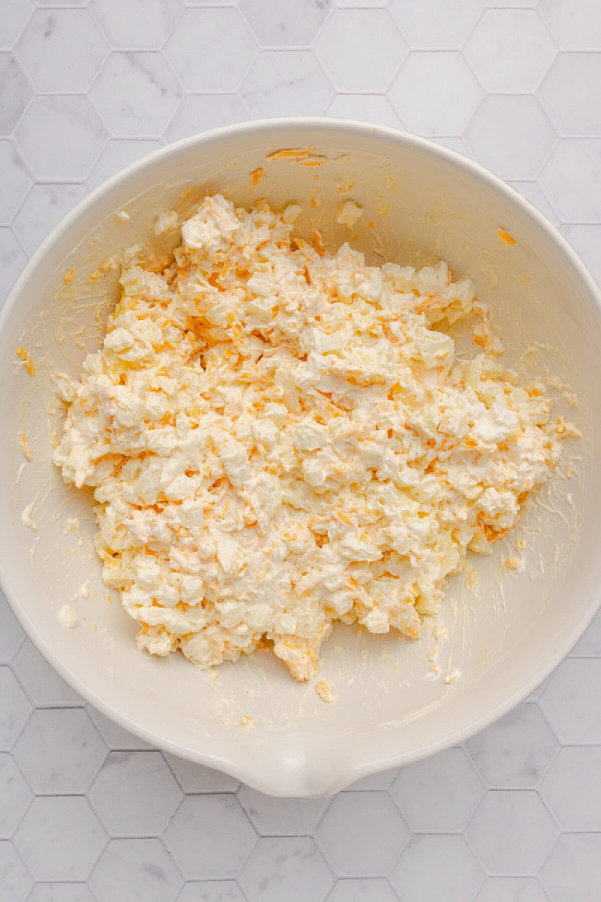 Frozen hash browns combined with sour cream, cream of chicken soup, salt, pepper, and Cheddar cheese in a mixing bowl.