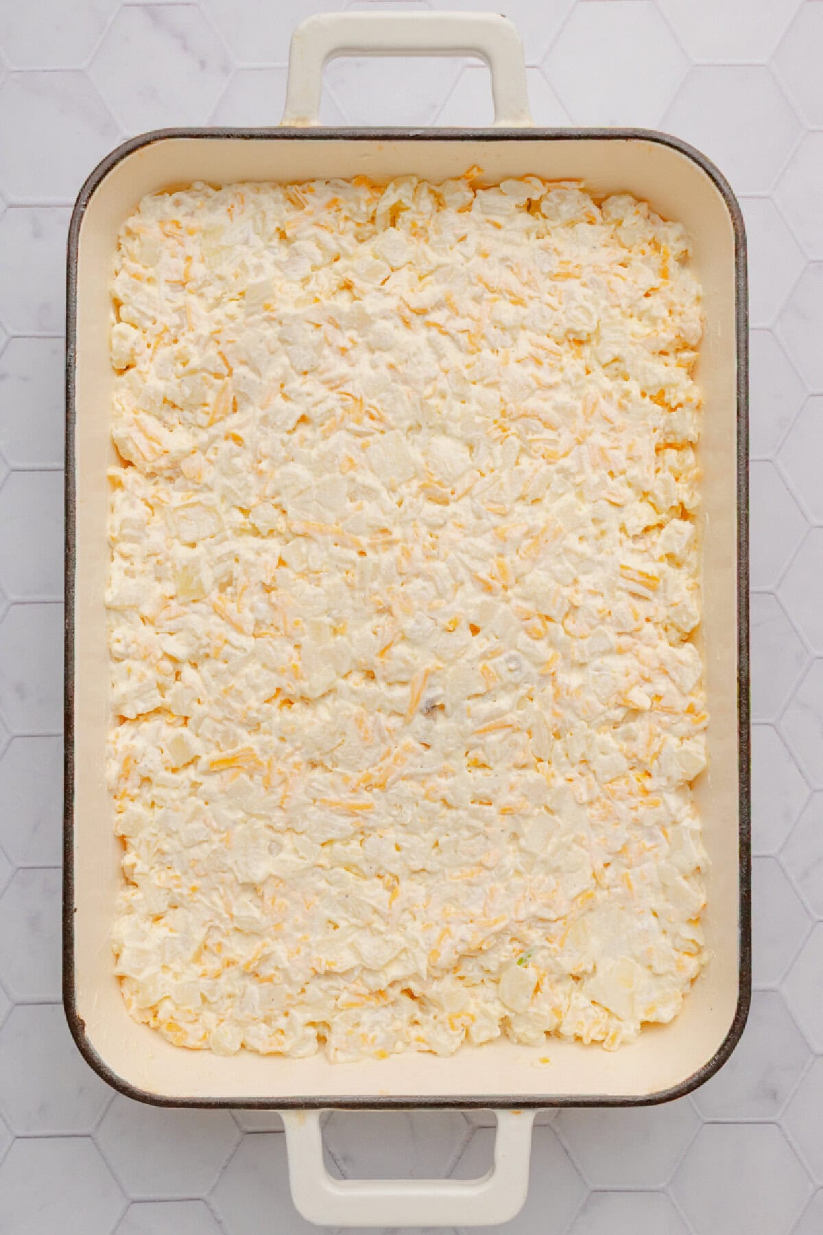 Hash browns combined with cream of chicken soup, sour cream, seasoning, and cheese and spread evenly into a baking dish.