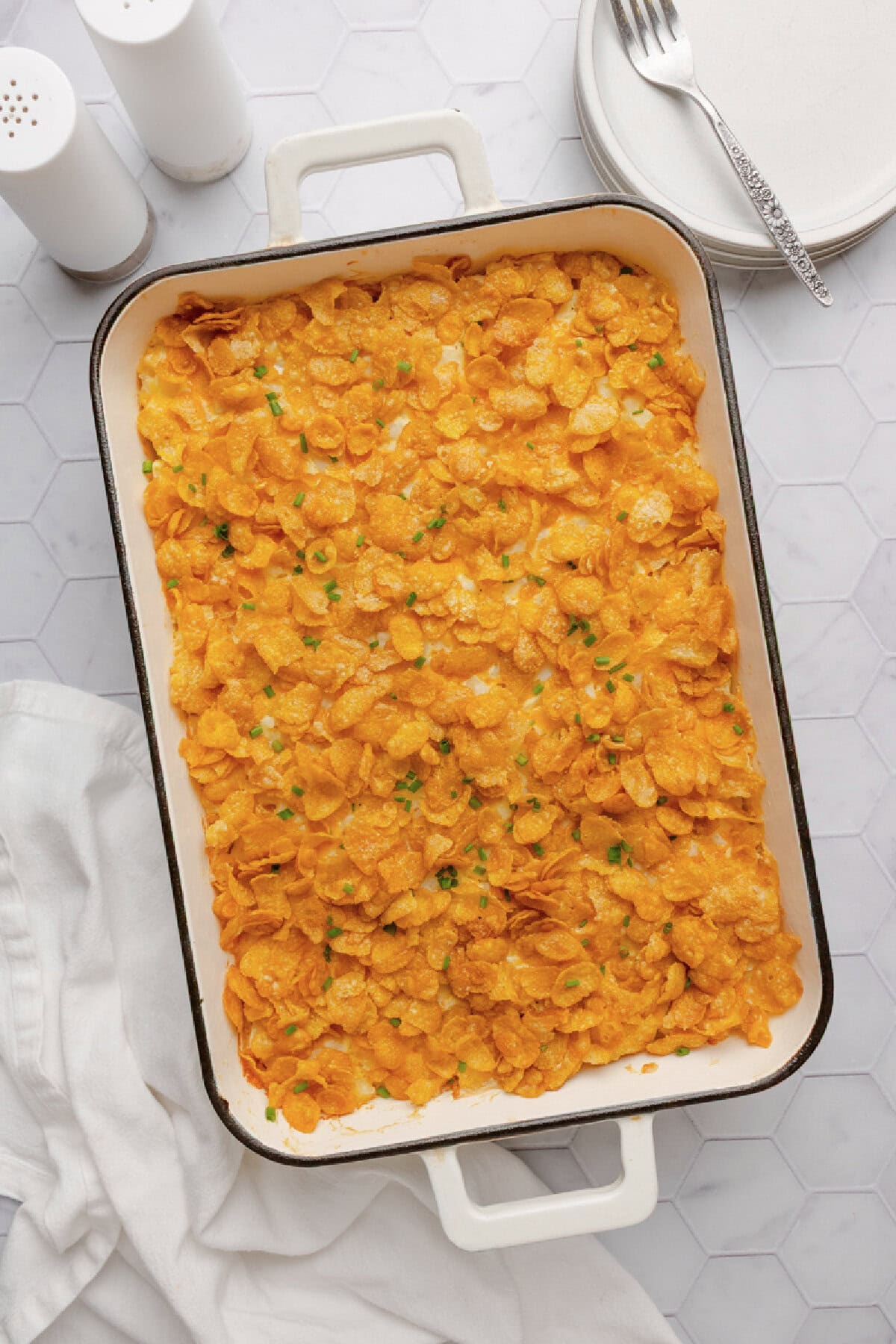 Funeral potatoes baked in a cream colored ceramic baking pan.