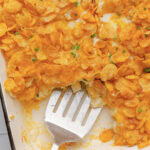 A metal spoon scooping a serving of hash brown casserole from a baking pan.
