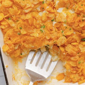 A metal spoon scooping a serving of hash brown casserole from a baking pan.