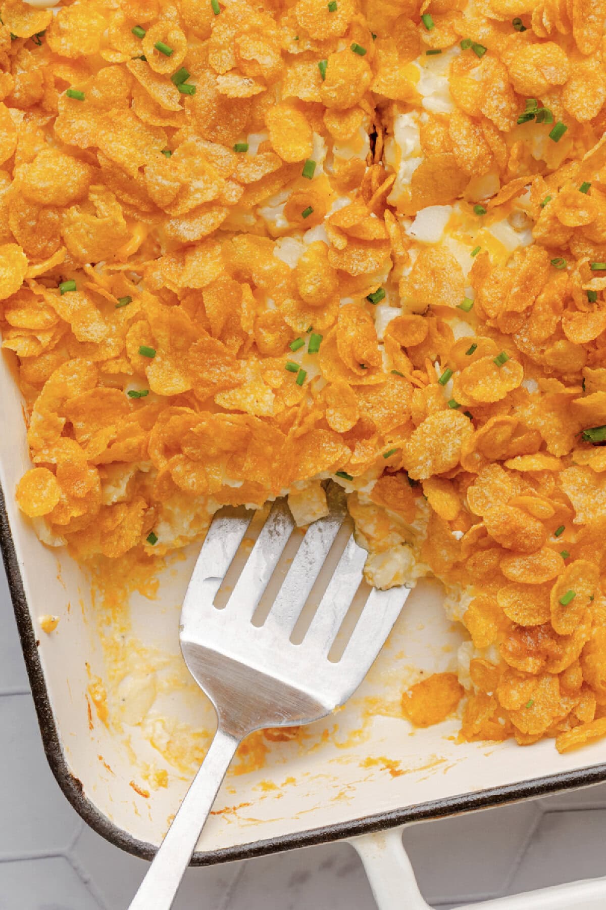 A metal spoon scooping a serving of hash brown casserole from a baking pan.
