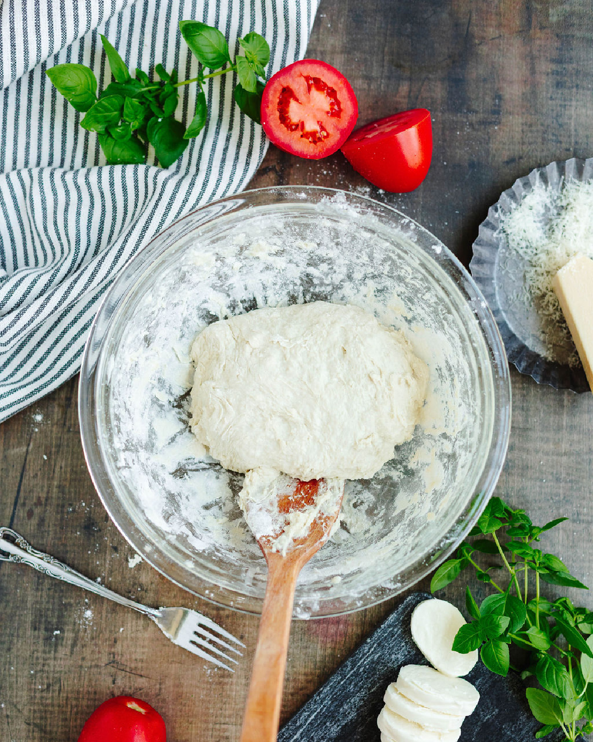 Pizza dough combined in a glass mixing bowl using a wooden spoon.