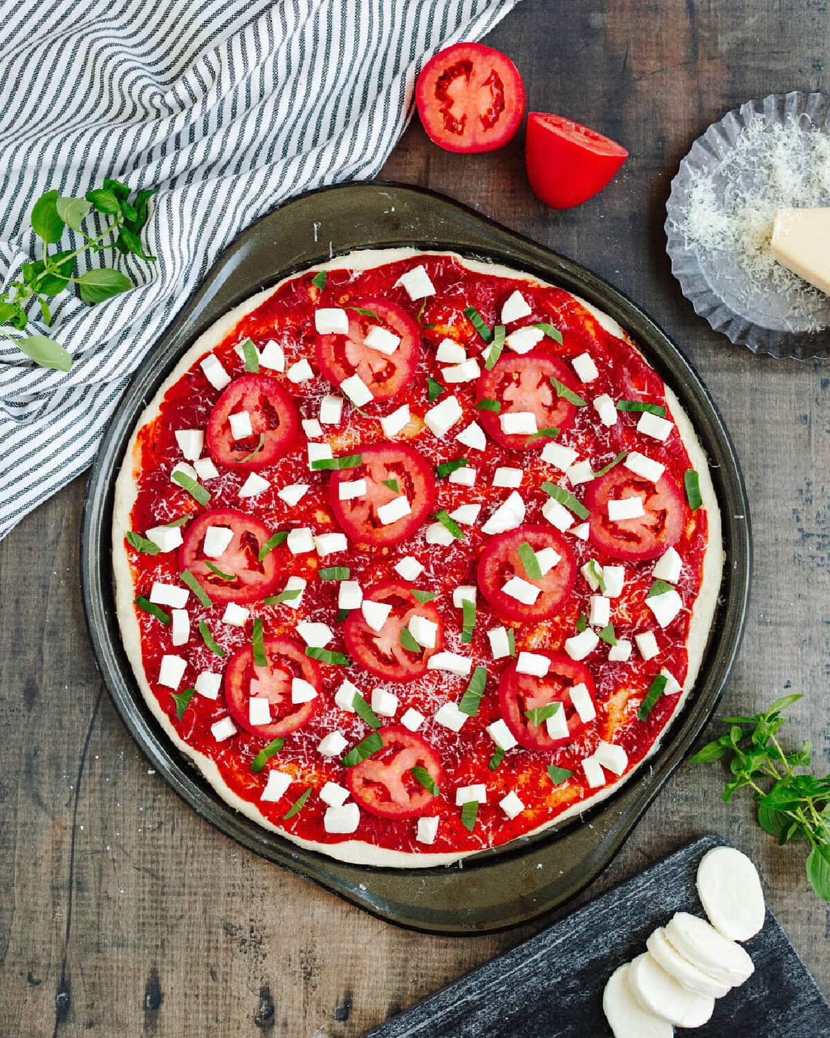 Fresh mozzarella, tomato slices, and basil over tomato sauce on a pizza crust.