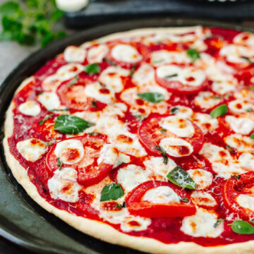 Baked pizza with tomato sauce, tomatoes, and basil.