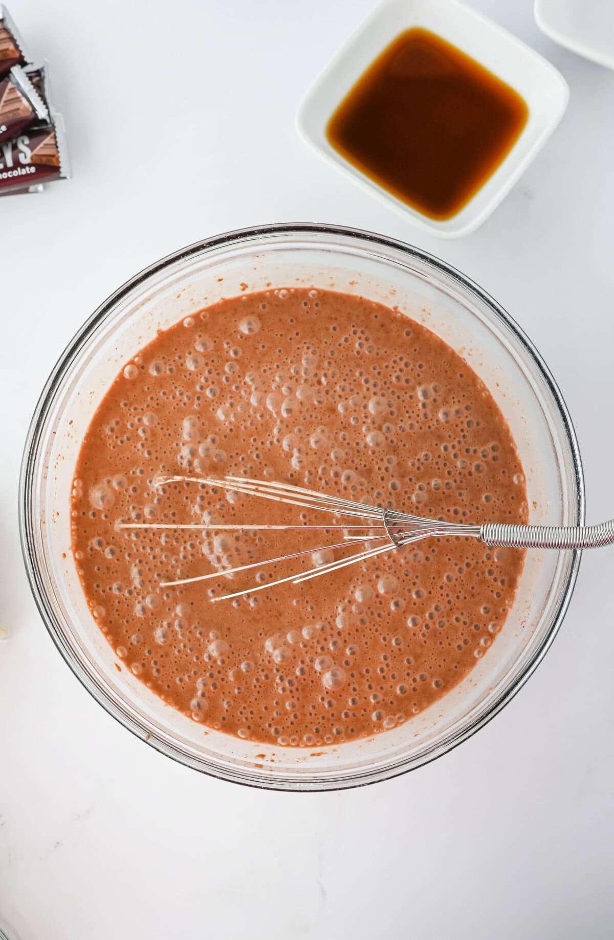 Chocolate pudding prepared in a glass mixing bowl using a whisk.