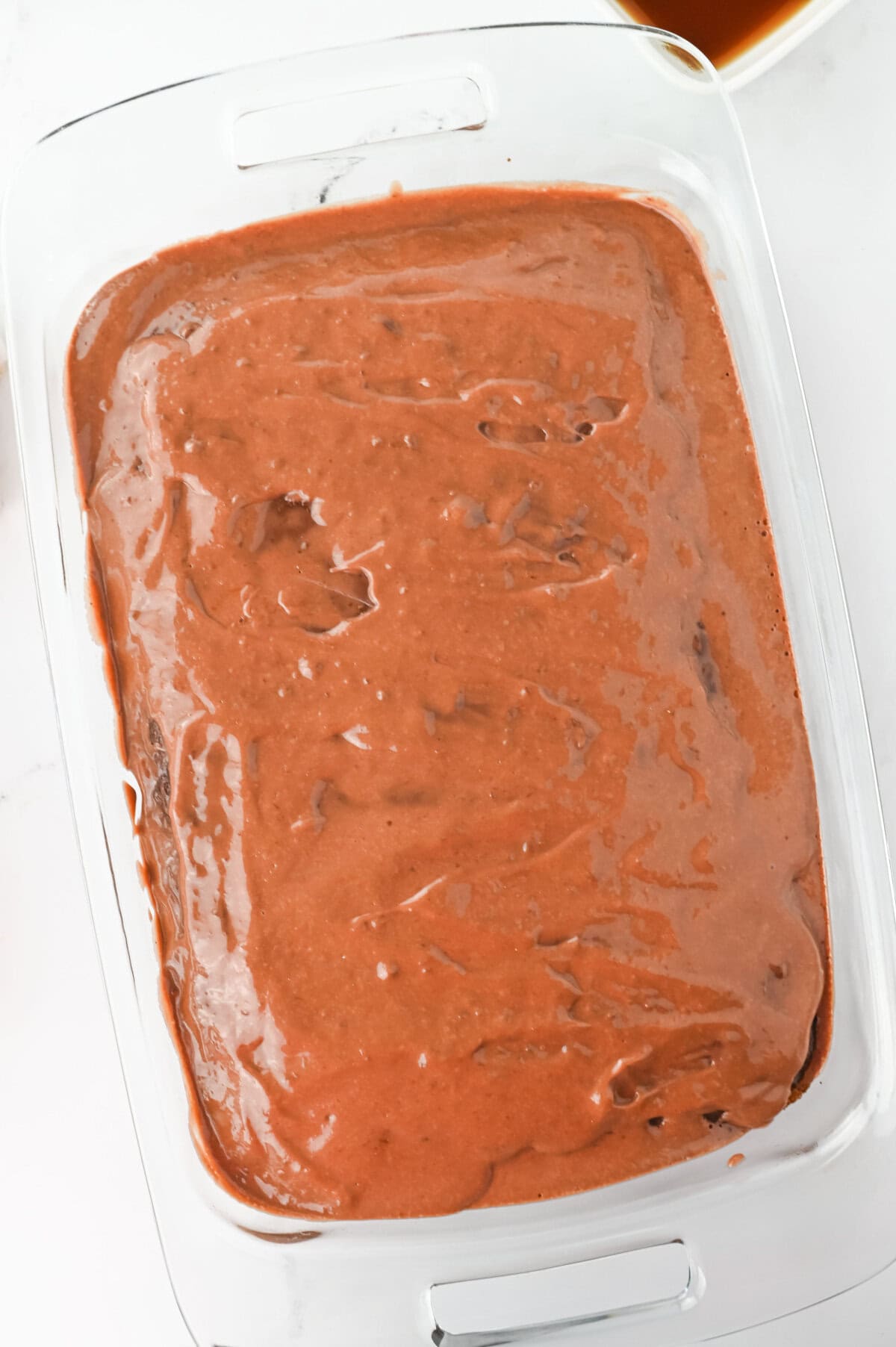 Chocolate pudding poured evenly on top of a chocolate cake.