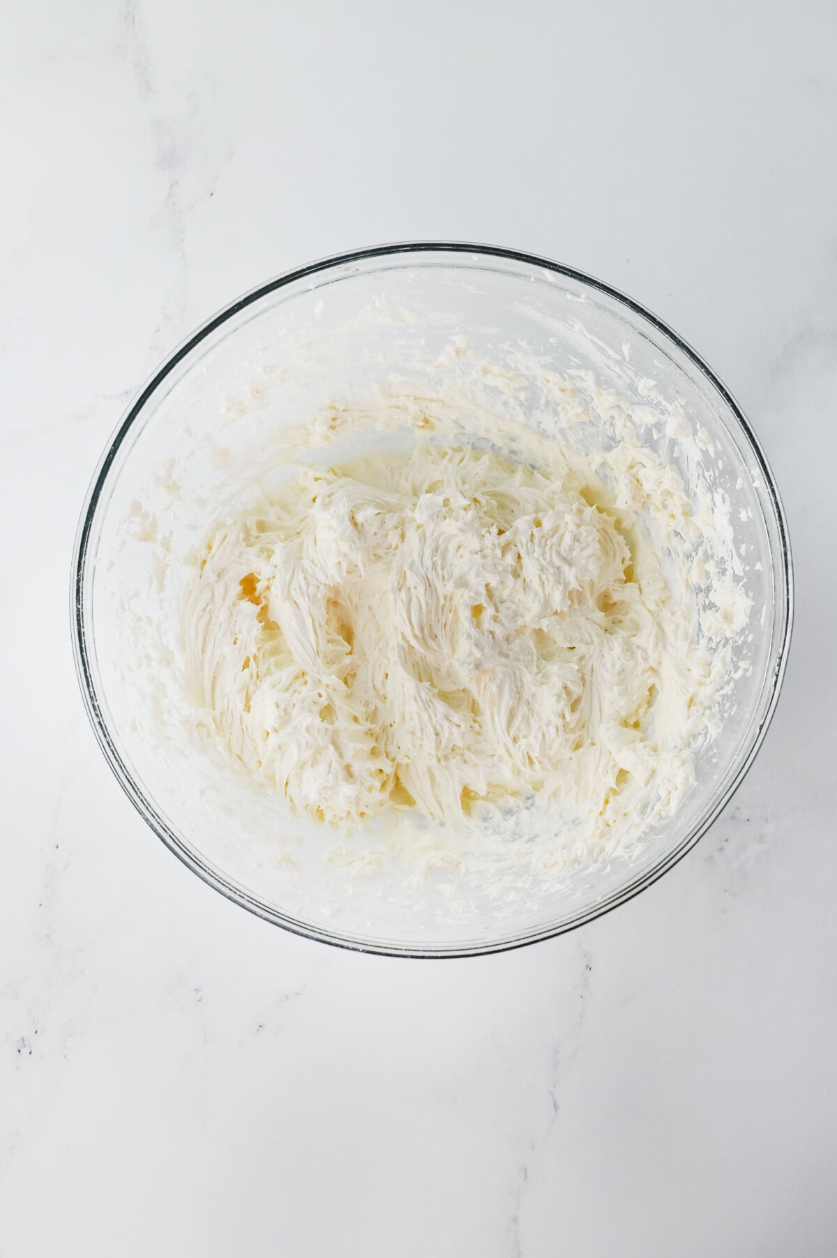 Marshmallow fluff, vanilla, and salt combined with powdered sugar in a glass mixing bowl.