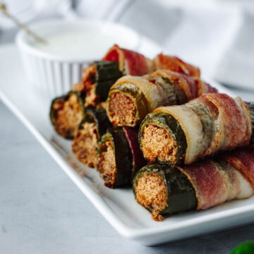 Crispy bacon wrapped jalapenos stuffed with goat cheese and honey on a white plate.