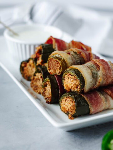 Crispy bacon wrapped jalapenos stuffed with goat cheese and honey on a white plate.