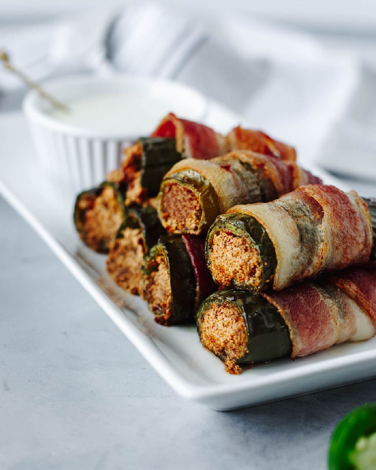 Crispy bacon wrapped jalapenos stuffed with goat cheese and honey on a white plate.