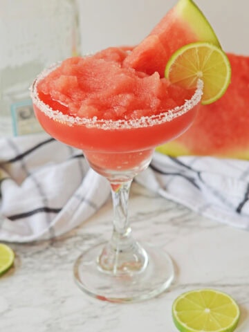 A watermelon margarita salt rimmed with a lime wedge and watermelon wedge.