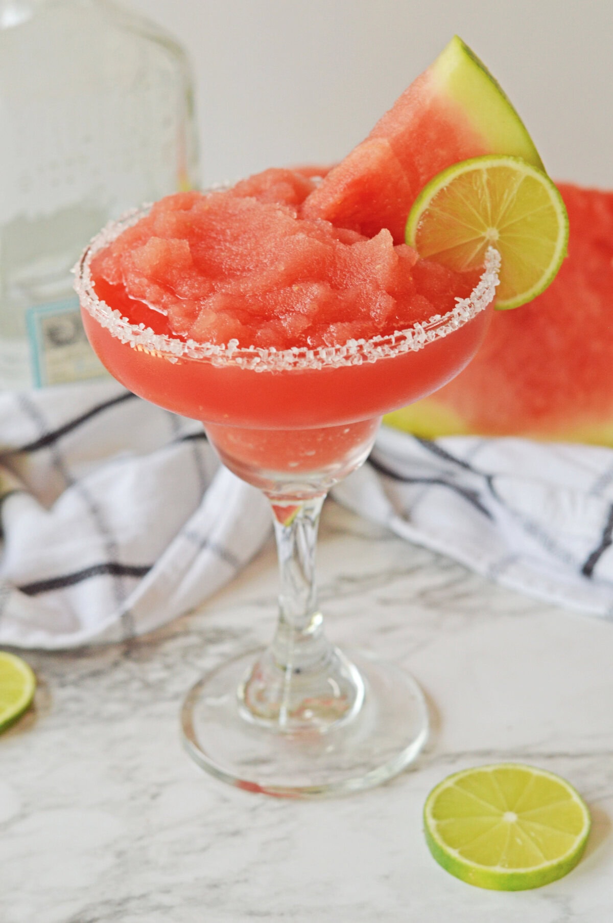 a frozen watermelon margarita in a glass with a salt rim and lime wedge.