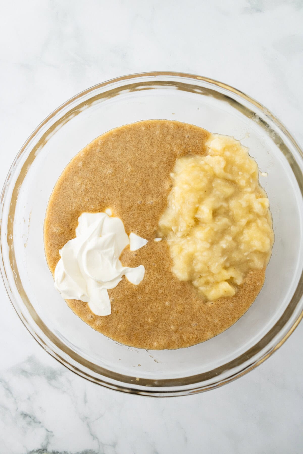 Banana and sour cream combined with wet ingredients in a mixing bowl.