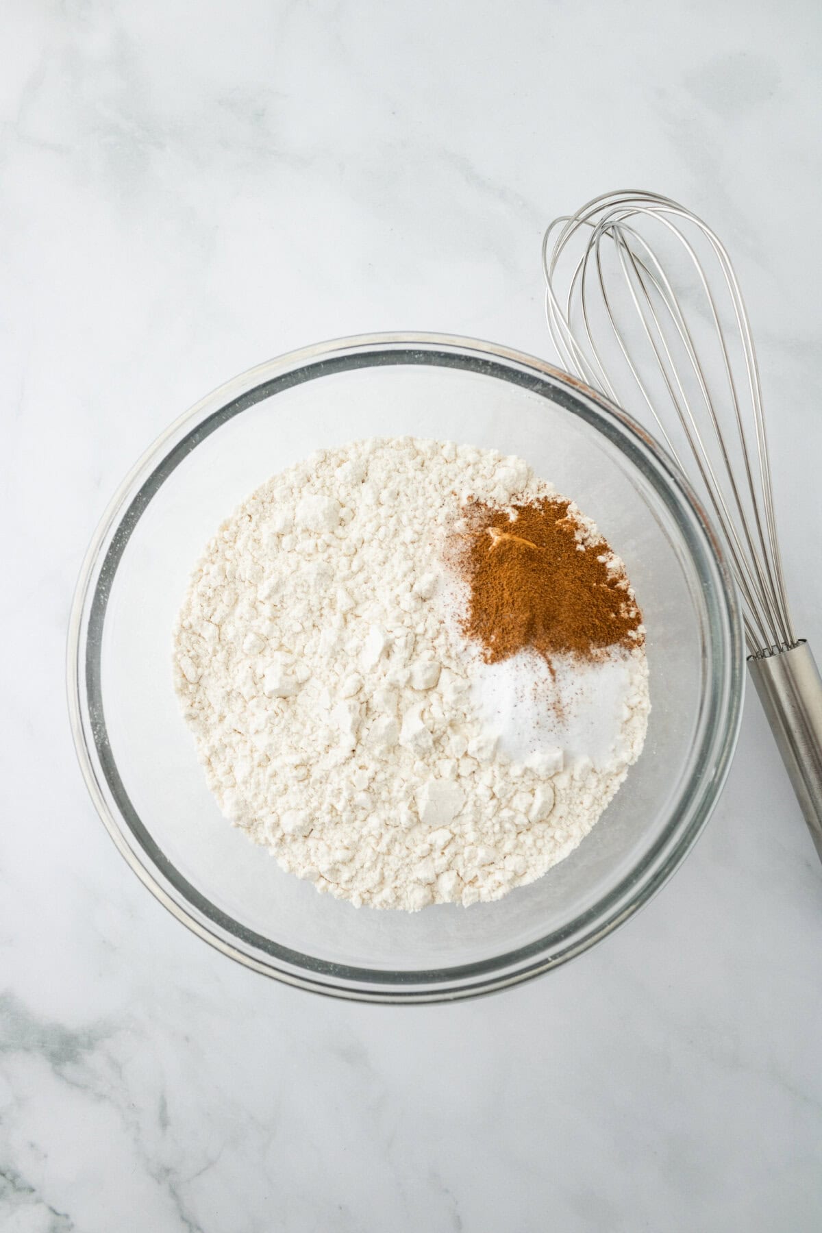 Flour, baking soda, cinnamon, and salt whisked together in a glass bowl.