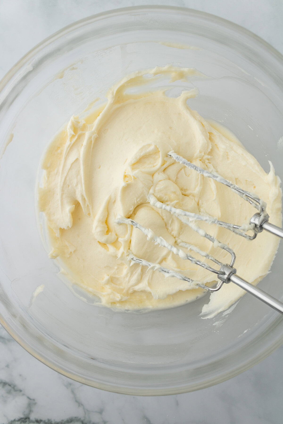 Cream cheese, butter, vanilla, and powdered sugar combined in a glass mixing bowl.