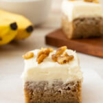 A cream cheese frosting topped dessert bar with walnuts on top.