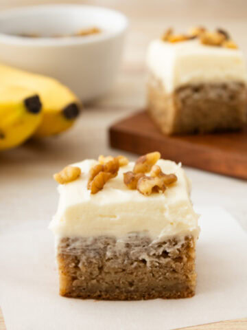 A cream cheese frosting topped dessert bar with walnuts on top.
