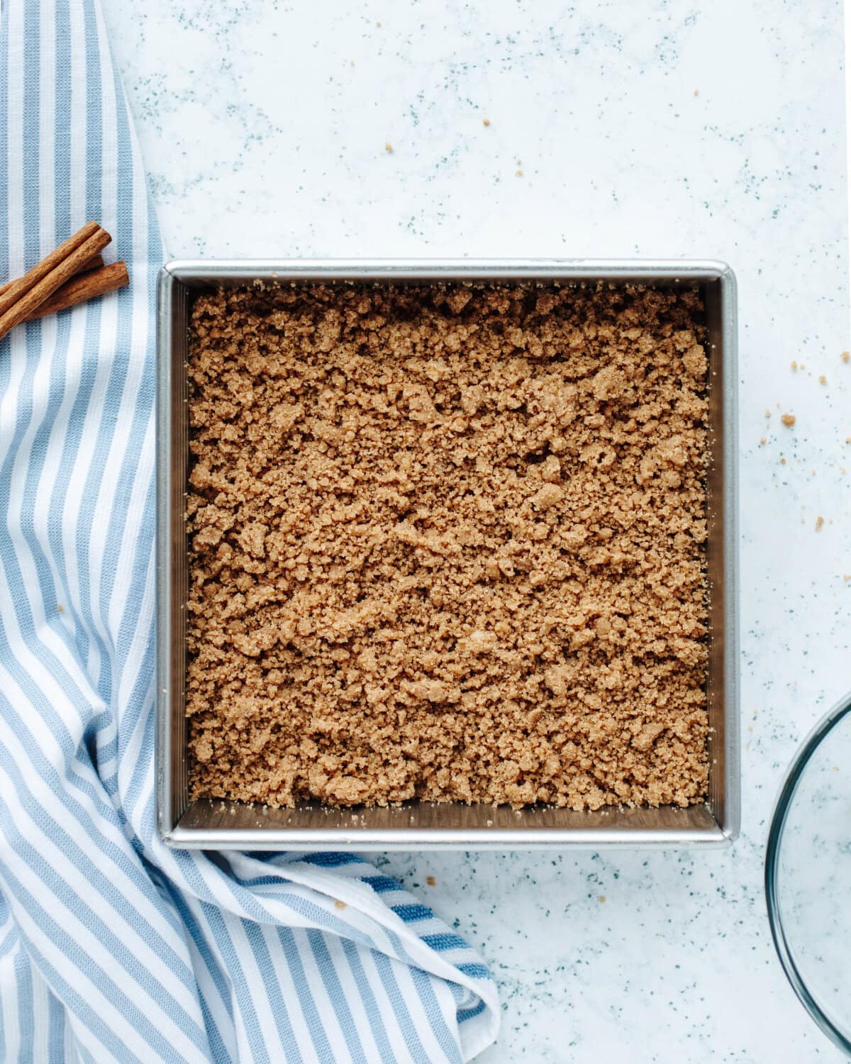 Cinnamon streusel sprinkled on top of the cake batter in an 8x8 baking pan.